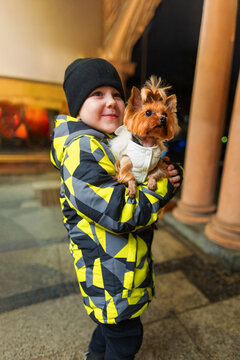 Child hold Yorkshire terrier outside in winter coat