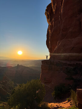 Hiker beneath towering red rock cliff at Arizona sunset