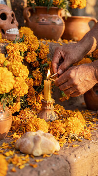 Weathered hands lighting beeswax candle among marigolds and skull on Day of the Dead altar