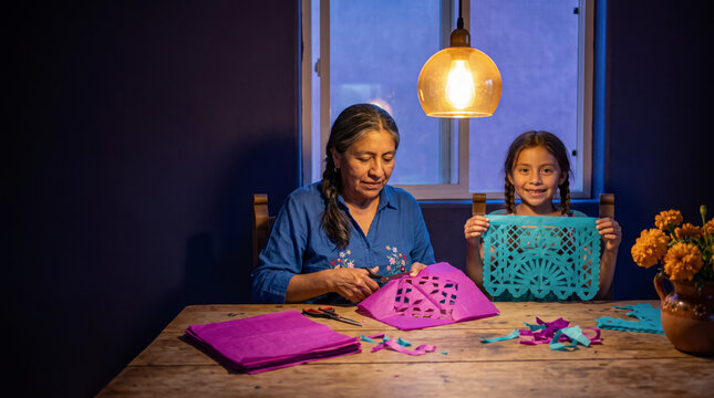 Engaged grandmother and granddaughter cutting paper banners for Mexico Day of the Dead