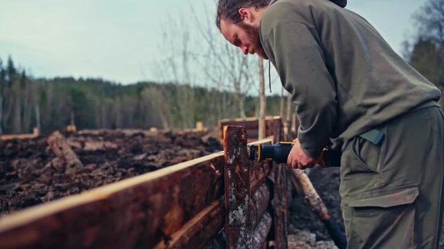 Man Uses A Cordless Power Tool To Cut Or Notch Stacked Wooden Planks During Outdoor Woodworking And Construction Work. Close-up Shot