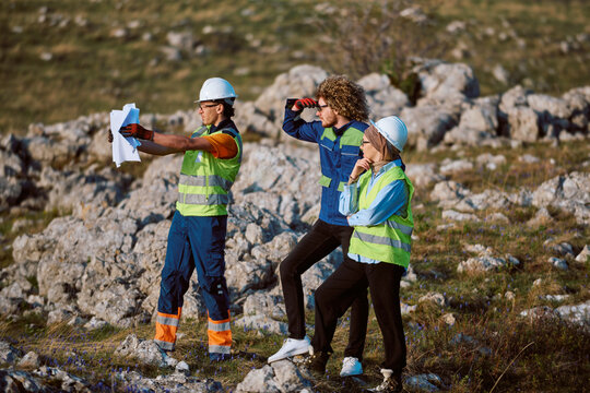 Civil Engineers and Surveyors in Safety Vests Reviewing Blueprints on Rocky Construction Site During Field Inspection
