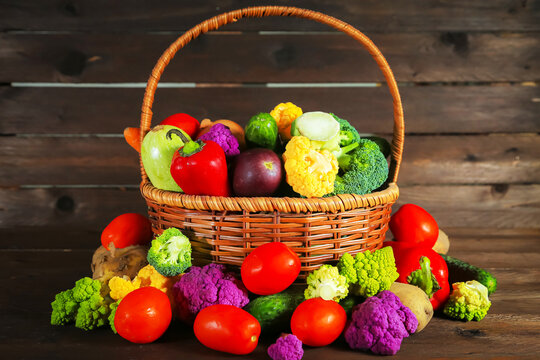 Fresh, shiny vegetables of various varieties in a wicker basket on a wooden background.