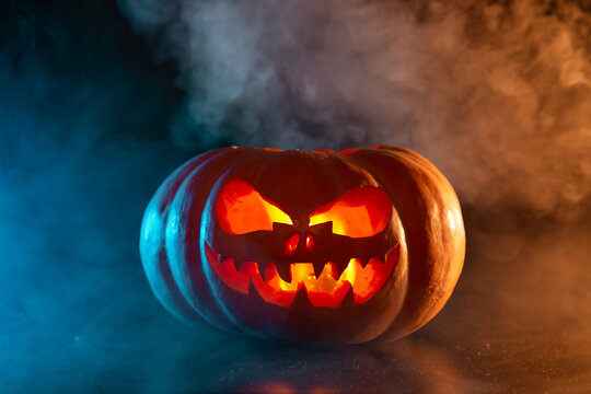 Halloween pumpkin with a scary glowing face in blue smoke.