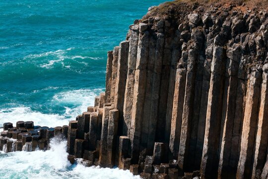 Columnar basalt formations along a rugged coastline with crashing waves