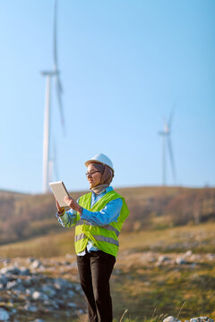 Female Engineer Wearing Hijab With Tablet At Wind Farm Inspecting Turbines For Renewable Energy