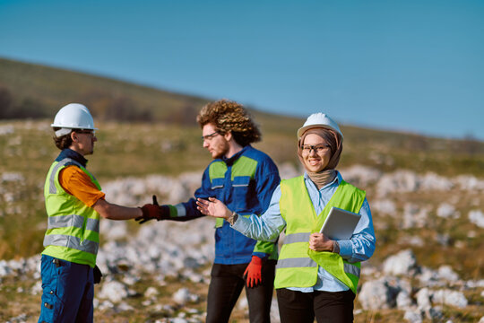 Diverse Engineers in Safety Gear Shaking Hands on a Rural Construction Site While Woman Holds Tablet