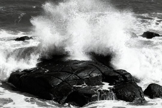 Waves crashing against dark rocks in a dramatic black and white coastal scene