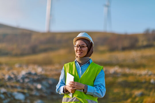 Female Engineer in Hard Hat and High-Vis Vest at Wind Farm Holding Tablet Overlooking Renewable Energy Site