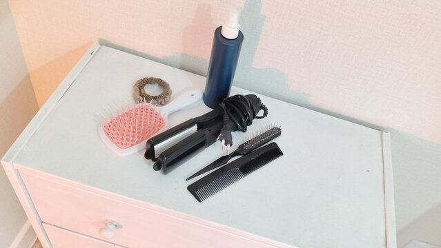 Hair styling tools and hair care products arranged on a dresser. Personal grooming and beauty routine. Haircare, hairstyling and cosmetic essentials. Home self-care concept.