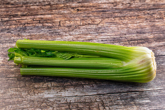 Fresh green celery stalks with leafy tops resting on rustic wooden surface showing natural texture and pale base