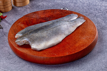Two raw seabass fillets with skin on resting on round wooden cutting board against gray textured surface © Andrei Starostin