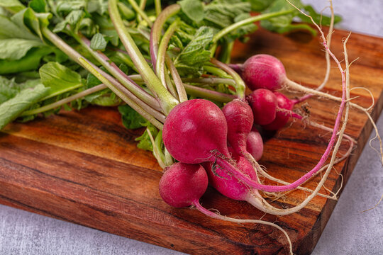 Fresh radishes with green leaves and roots on dark wooden cutting board