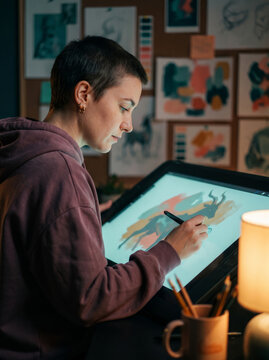 Young female digital artist drawing on a tablet in a dark studio, ideal for creative focus and concept design career concepts.