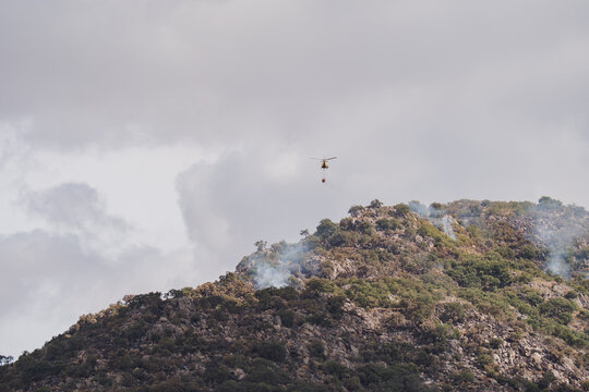 Firefighting helicopter drops water over smoky hillside