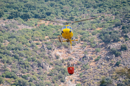 Firefighting helicopter carry water bucket over wildfire terrain