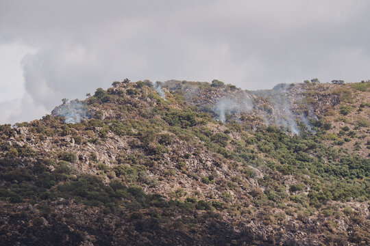 Wildfire smoke rises over rocky mountainous landscape