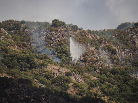 Firefighting helicopter perform water drop over hillside wildfire