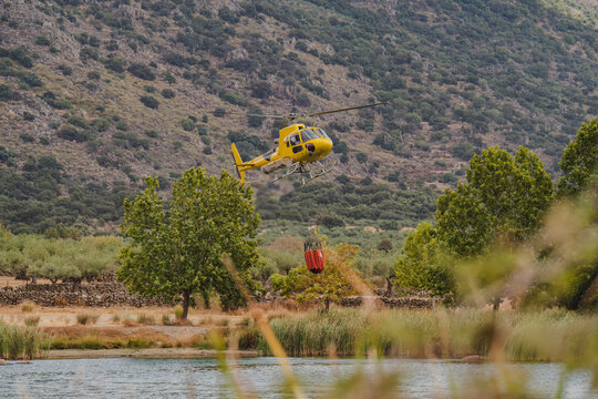 Yellow firefighting helicopter collect water near wildfire