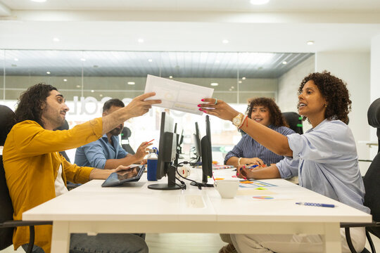 Coworking office team exchange document across shared desk
