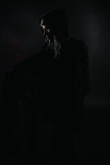 A hooded woman posed in a dark low-key portrait with a dramatic side silhouette. The moody scene emphasizes mystery and solitude in minimalist studio lighting. © qunica.com