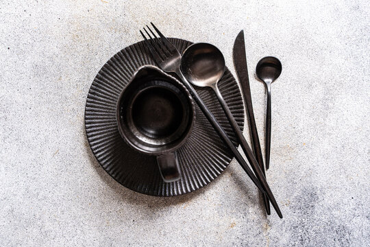 Black tableware and cutlery arranged on textured table