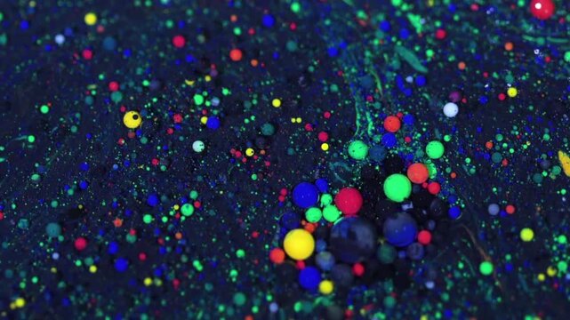 An artistic movement of colorful fluids and shimmering paint bubbles against a dark background. 