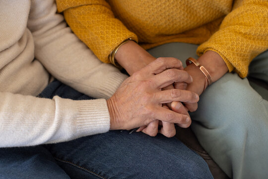 Senior Asian man, African woman in knit sweaters sitting on sofa holding interlocked hands