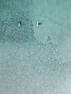 Aerial view of two surfers on surfboards in the clear turquoise waters of the Lofoten archipelago in Svolvaer, Nordland, Norway.