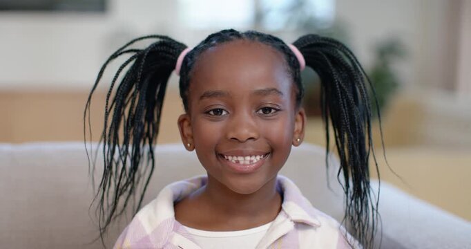 African female child reacting to camera smiling widening grin on armchair at home showing tooth gap