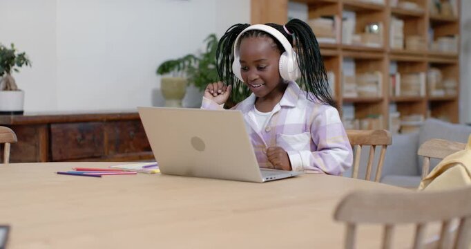 African American child in plaid shirt wearing white headset raising fist after laptop ping, typing
