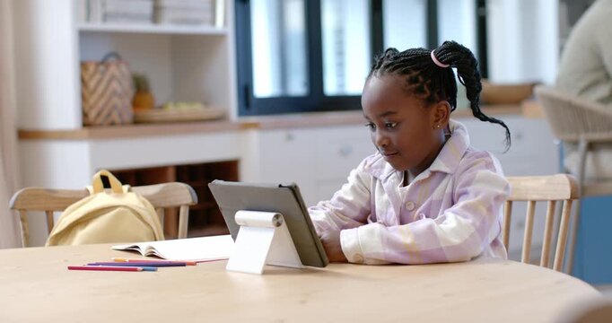 Female child sitting at kitchen table, tablet on stand drawing focus, tapping screen