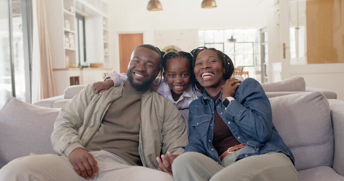 African family on couch laughing as teen daughter moving from behind to join parents holding hands