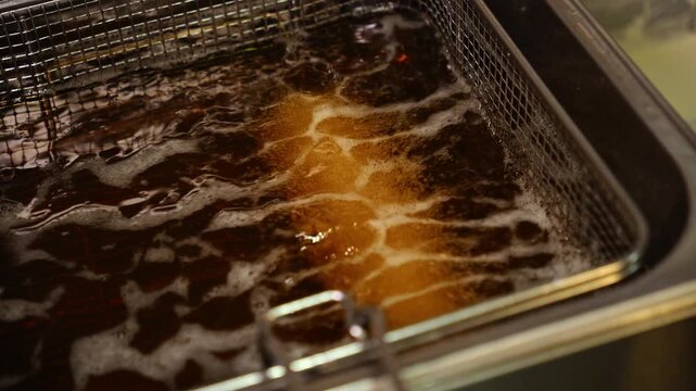 Tempura sushi roll fries in bubbling hot oil inside a commercial deep
