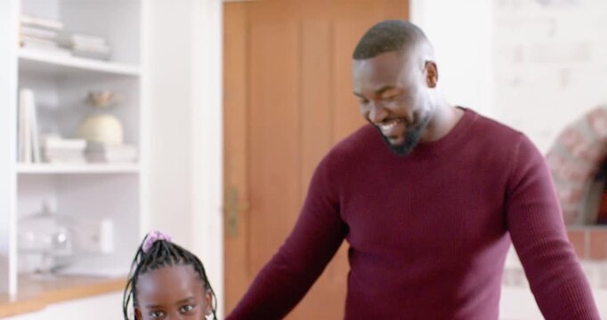 Father teaching youth daughter at home kitchen counter, gesturing toward pizza bases and mushrooms