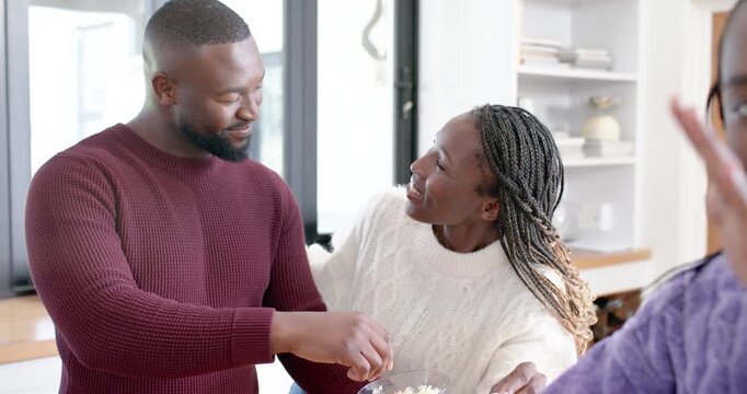 African family man sprinkling cheese making pizza after woman offering bowl at kitchen island
