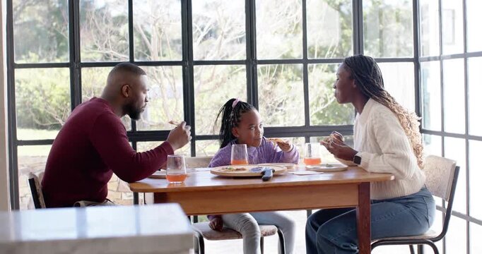 African American family during meal at wood table by window, mother talking, father sipping juice
