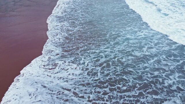 Aerial beach footage showing a clean line of white surf advancing over dark wet sand, with smooth wave textures and tranquil coastal movement.