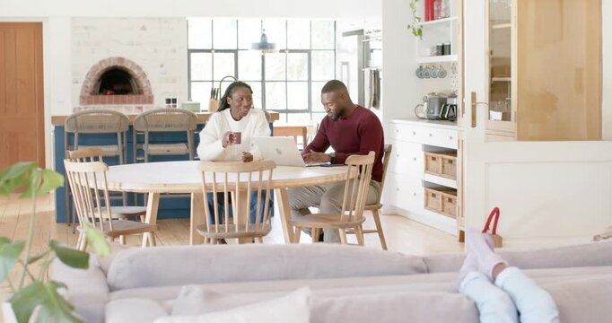 African couple coordinating laptop and phone work at table as child staying occupied on tablet