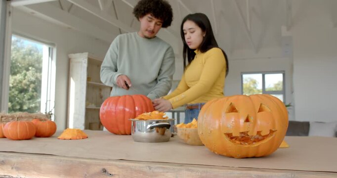 African American couple carving pumpkins together using knife and bowl at home for halloween