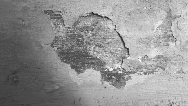 Weathered plaster wall with an irregular exposed patch, peeling paint, rough texture and layered surface marks. Monochrome grunge background for architectural and abstract use.