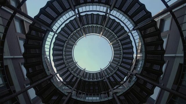 Rotating camera filming spiral staircase in atrium, showing inner rings, treads and sky opening