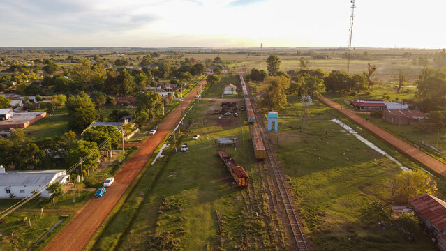 Aerial view of the rural town of Guaviravi, featuring a railway line with freight cars, dirt roads, scattered houses, and a windmill in Guaviravi, Corrientes Province, Argentina.