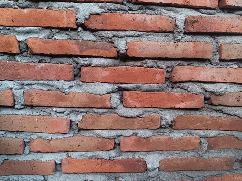 Old red brick wall with rough gray mortar, weathered surface and rustic texture, creating a natural architectural background for construction, design and vintage concepts.