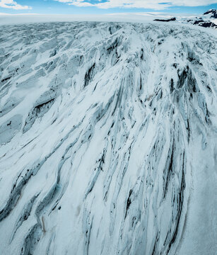 Aerial view of Vatnajokull glacier featuring deep crevasses, textured ice formations, and snow-covered slopes under a clear sky in Iceland.