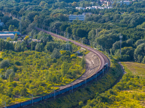 Aerial view of a freight train traveling along an elevated railway viaduct winding through a lush green forest and surrounding vegetation, Poznan, Greater Poland Voivod, Poland.