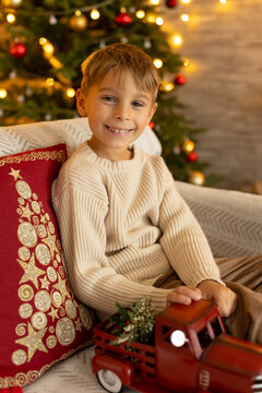 Cute preschool boy, sitting in front of the fireplace, holding christmas present and reading a book, joy and happiness
