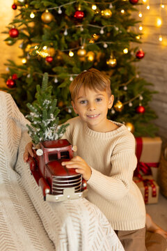 Cute preschool boy, sitting in front of the fireplace, holding christmas present and reading a book, joy and happiness