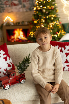 Cute preschool boy, sitting in front of the fireplace, holding christmas present and reading a book, joy and happiness
