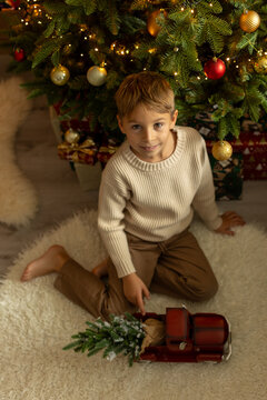 Cute preschool boy, sitting in front of the fireplace, holding christmas present and reading a book, joy and happiness